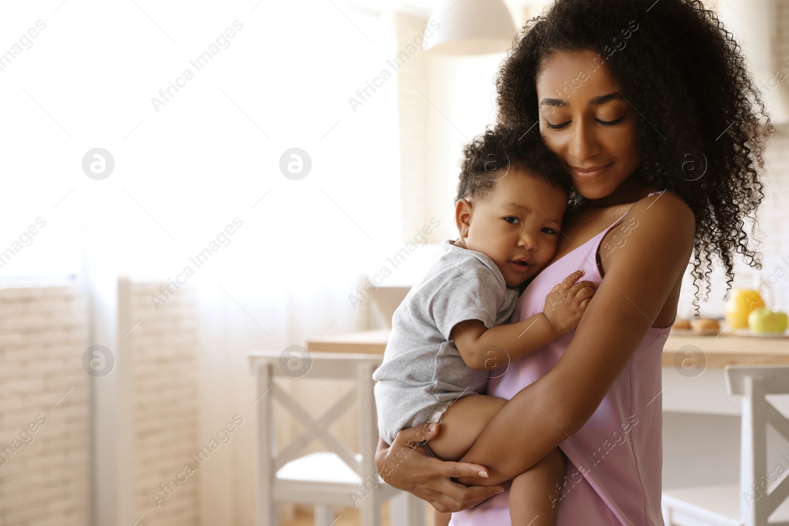 Photo of African-American woman with her baby in kitchen. Happiness of motherhood