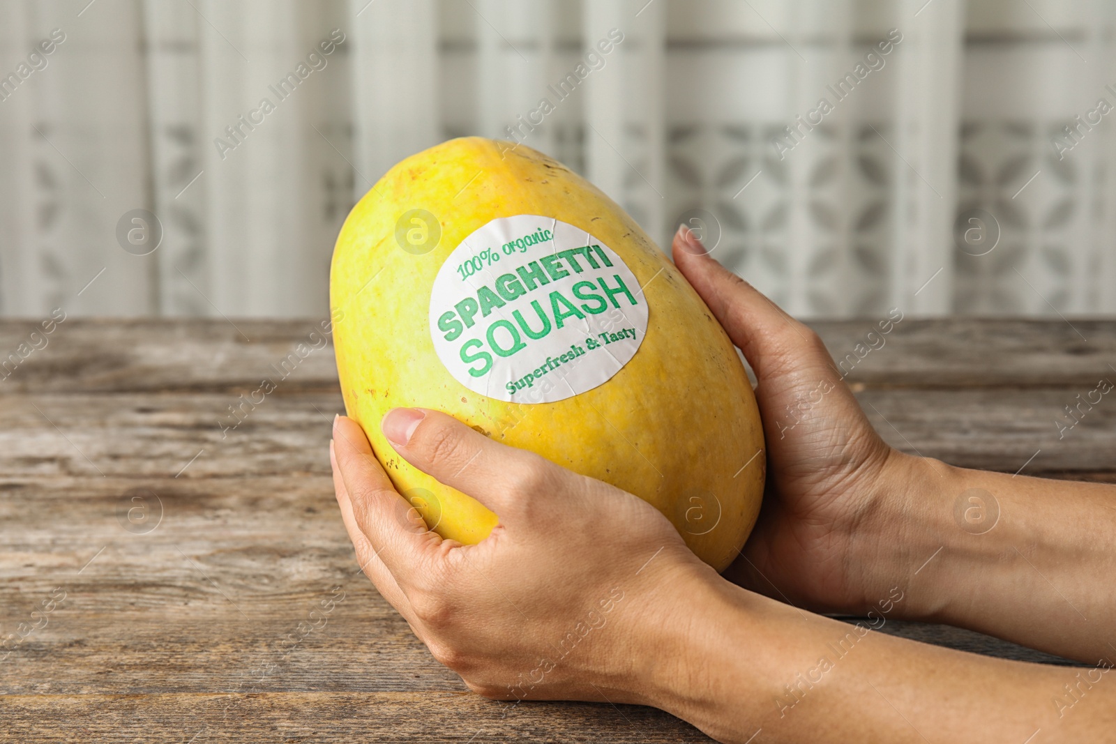 Photo of Woman holding ripe spaghetti squash on wooden table, closeup