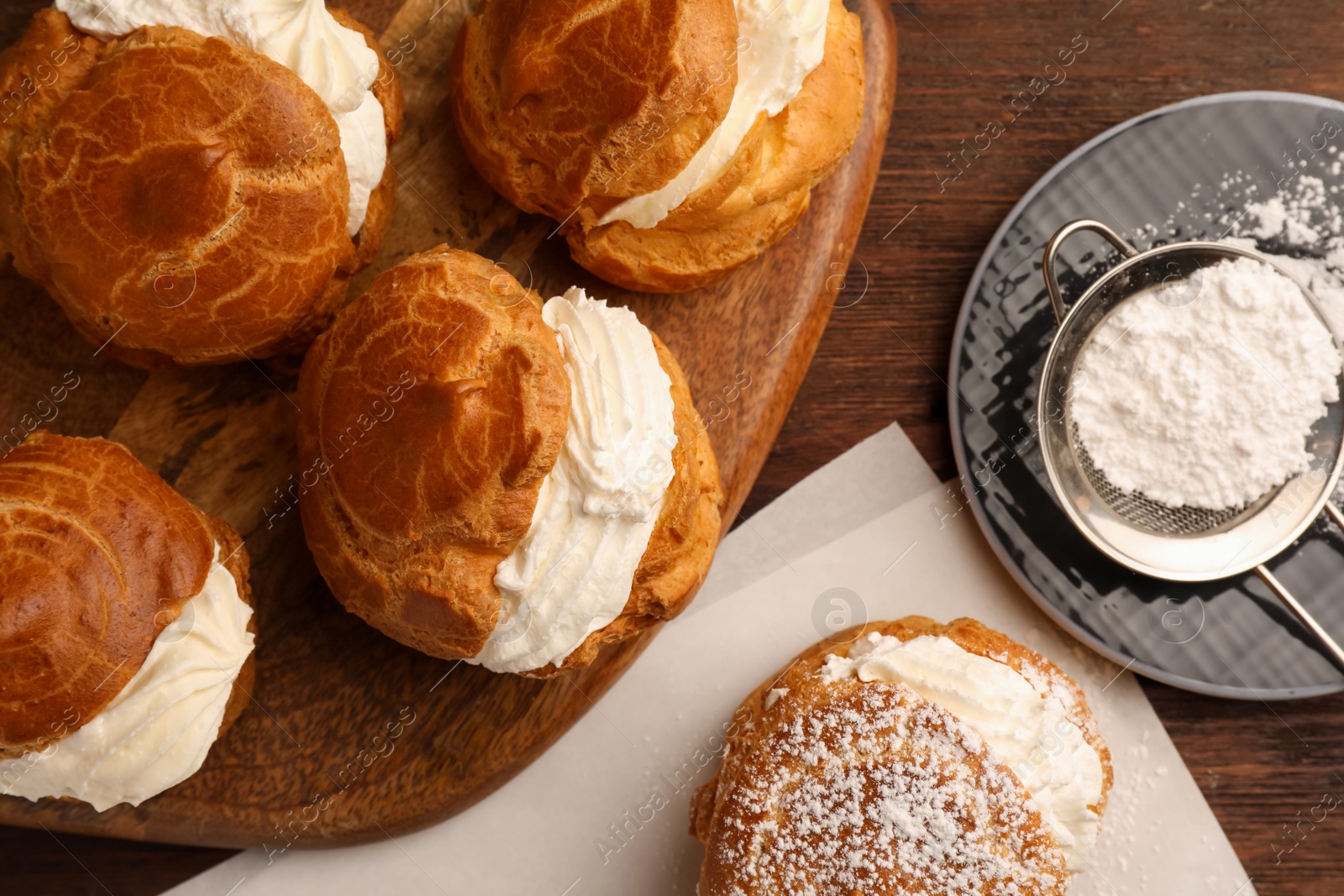 Photo of Delicious profiteroles with cream filling and powdered sugar on wooden table, flat lay
