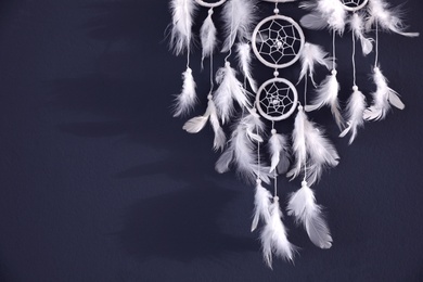 Photo of Beautiful dream catcher hanging on dark blue wall, closeup. Space for text