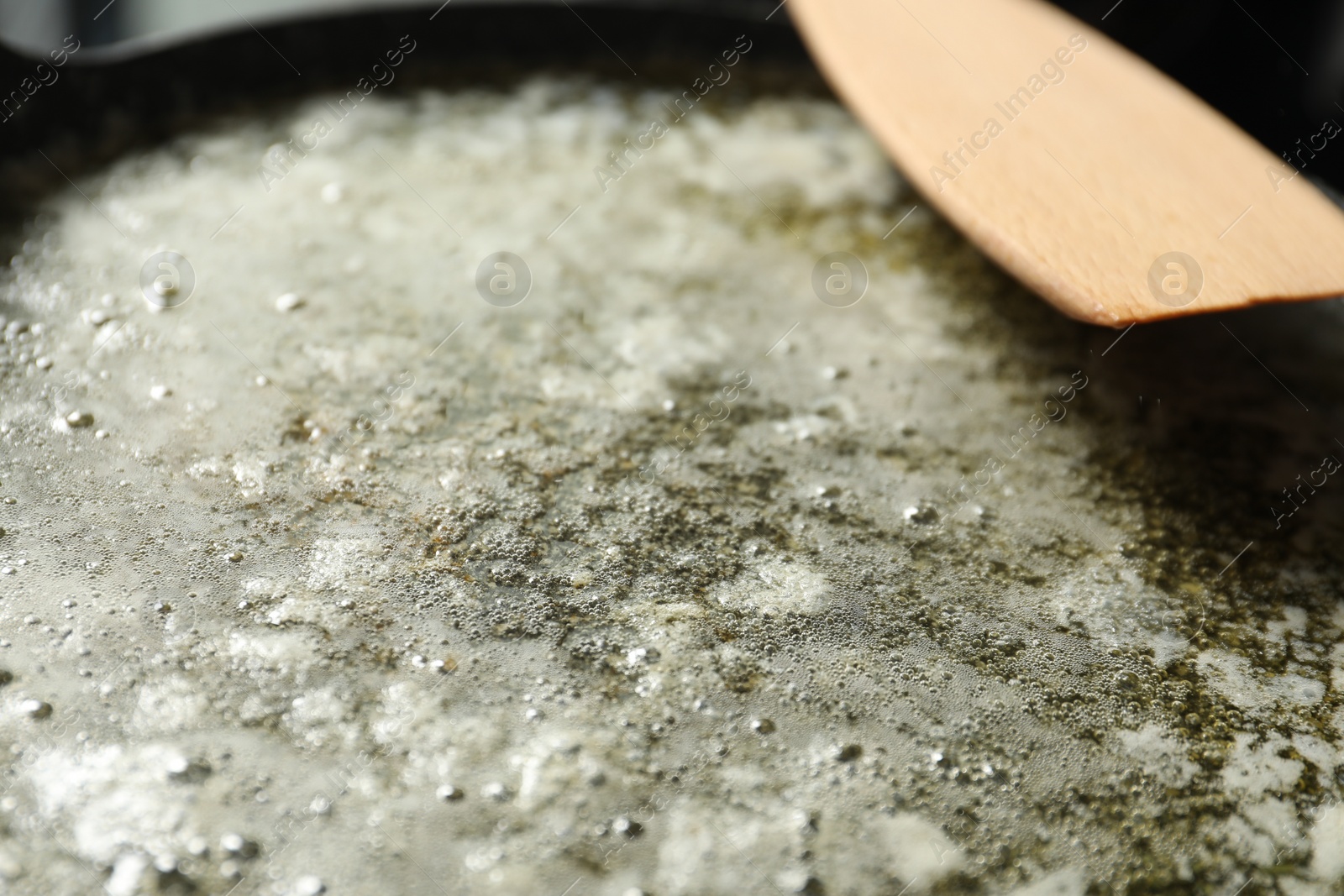 Photo of Melted butter in frying pan and wooden spatula, closeup