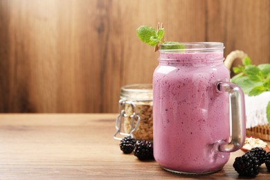 Delicious blackberry smoothie in mason jar and berries on wooden table. Space for text