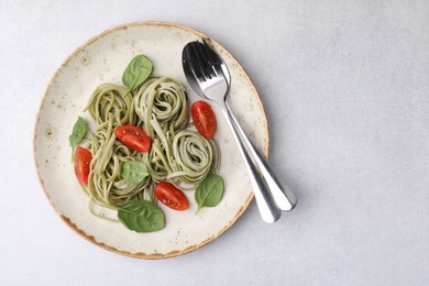 Photo of Tasty pasta with spinach, tomatoes and cutlery on light grey table, top view. Space for text