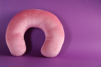 Photo of Pink travel pillow on violet background, space for text