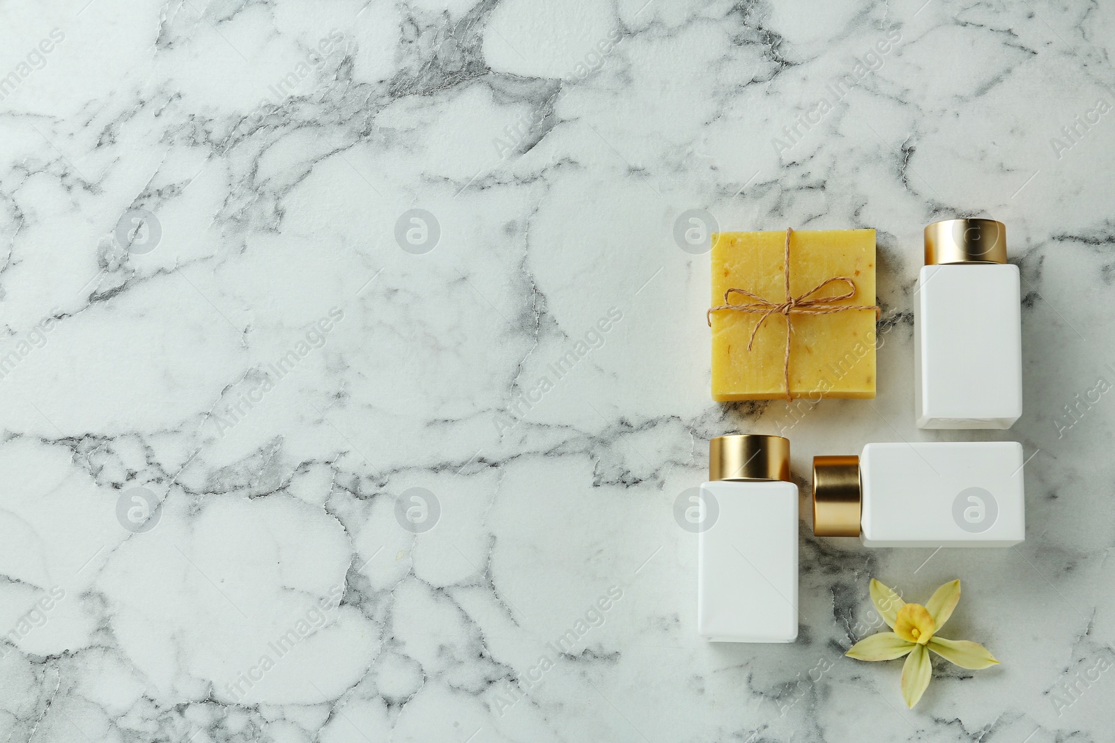 Photo of Cosmetic bottles, flower and handmade soap on marble table, flat lay with space for text. Spa treatment