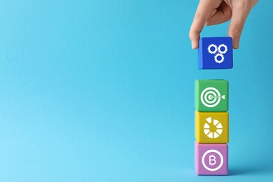 Closeup view of woman stacking colorful cubes with different images on light blue background, space for text. Management concept