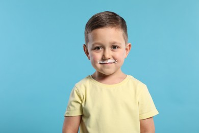 Cute boy with milk mustache on light blue background