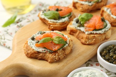 Tasty canapes with salmon, capers, cucumber and sauce on table, closeup