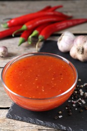 Photo of Spicy chili sauce in bowl and ingredients on wooden table, closeup