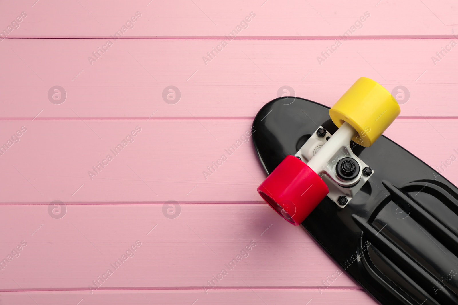 Photo of Black skateboard on pink wooden background, top view. Space for text