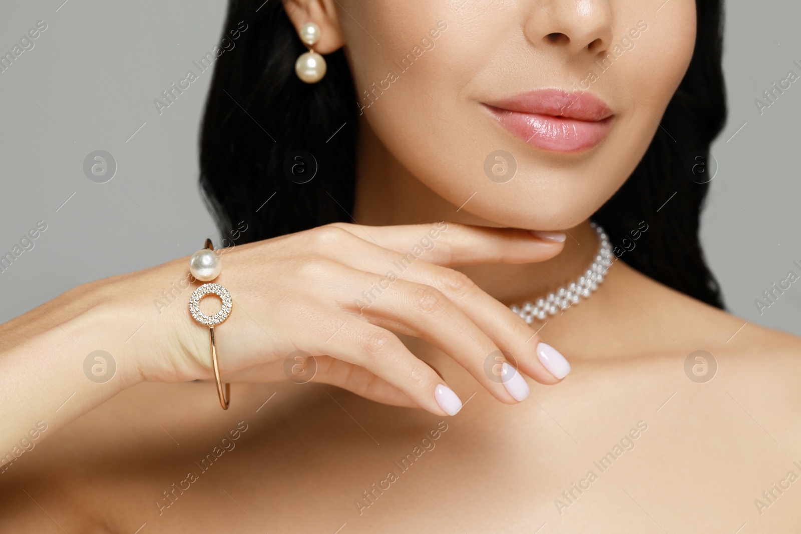 Photo of Young woman wearing elegant pearl jewelry on grey background, closeup