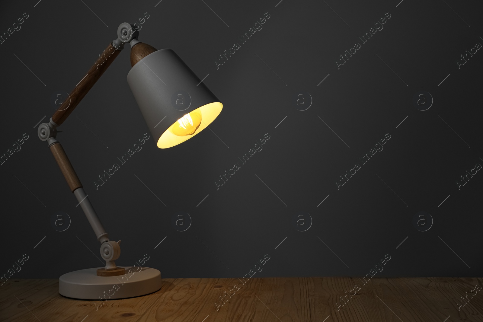 Photo of Stylish modern desk lamp on wooden table at night, space for text