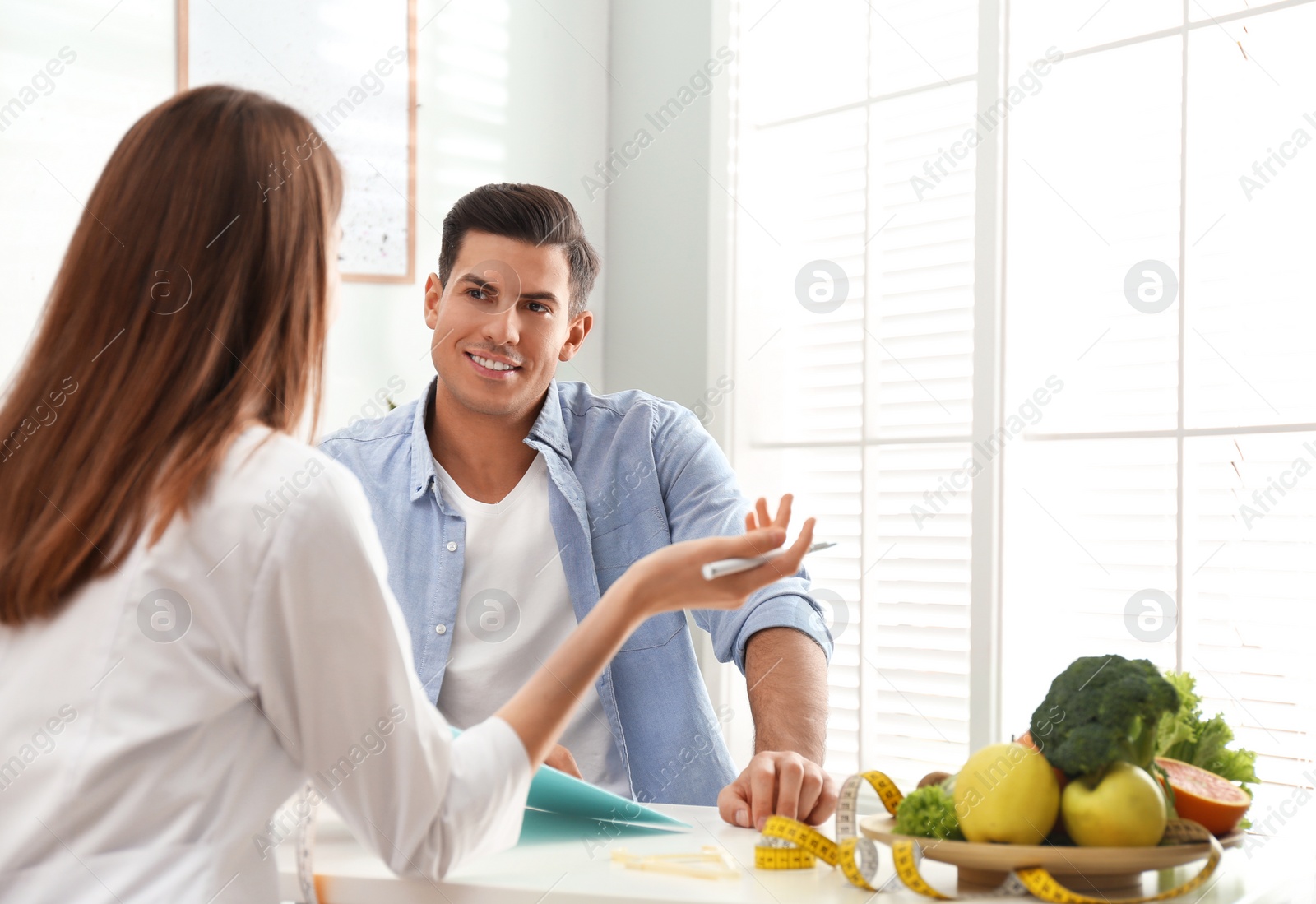 Photo of Young nutritionist consulting patient at table in clinic