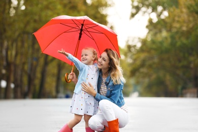 Happy mother and daughter with red umbrella on street