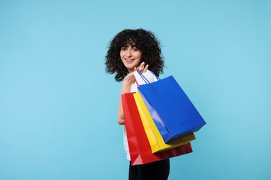 Happy young woman with shopping bags on light blue background. Space for text