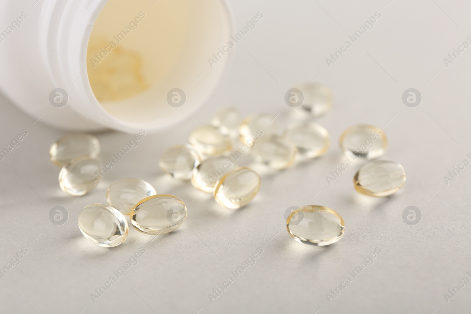 Photo of Vitamin capsules and bottle on light grey background, closeup