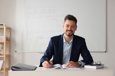 Photo of Happy teacher sitting at table in classroom
