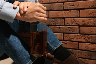 Addicted man with bottle of alcoholic drink near red brick wall, closeup