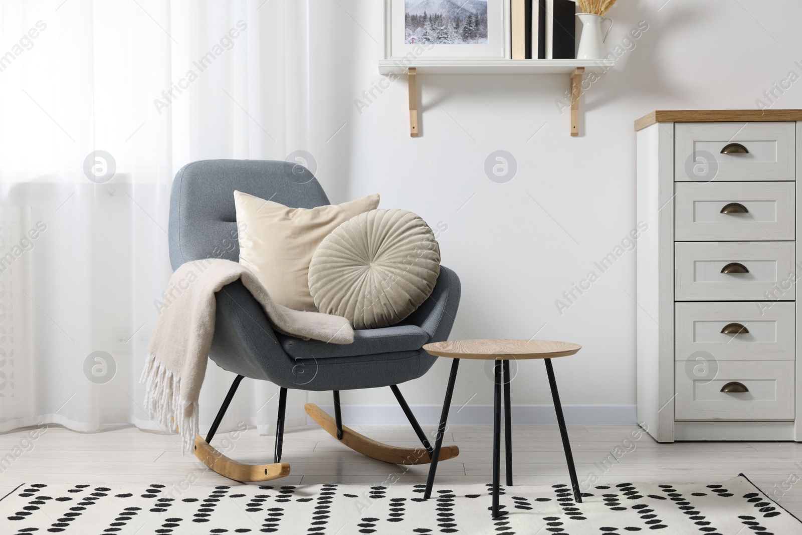 Photo of Soft pillows and blanket on rocking armchair indoors