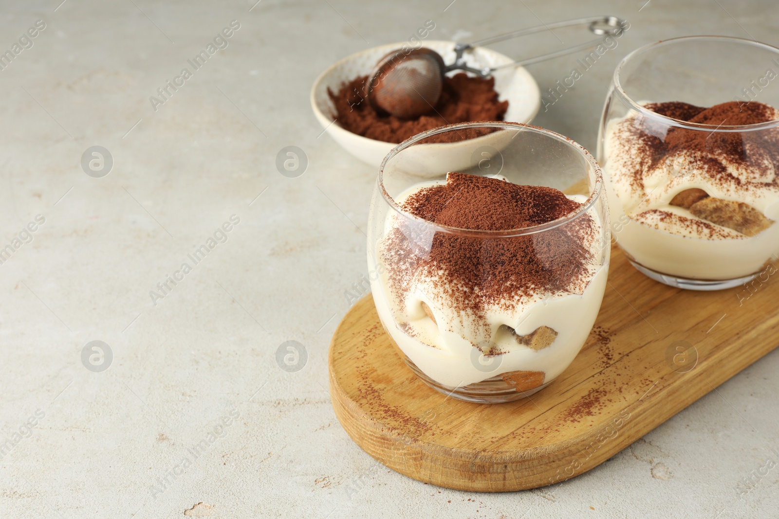 Photo of Delicious tiramisu in glasses on light table, Space for text