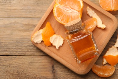 Photo of Bottle of tangerine essential oil and peeled fresh fruit on wooden table, flat lay. Space for text