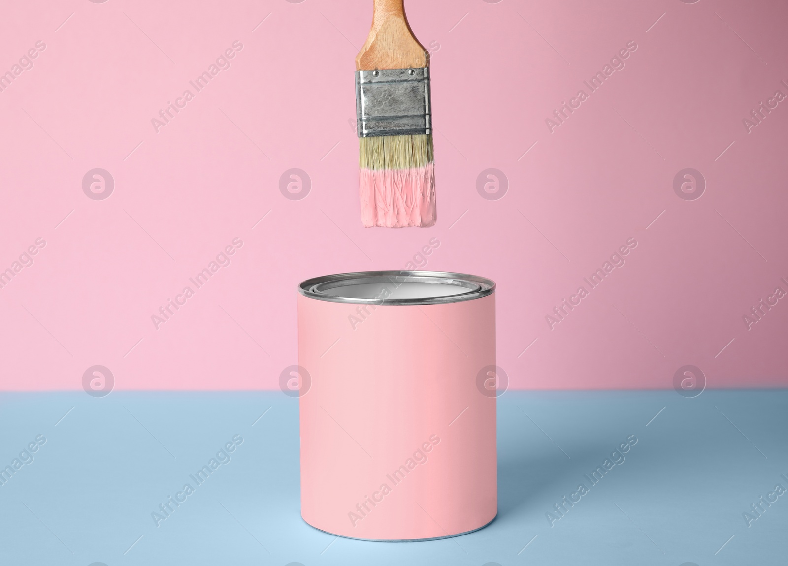 Photo of Brush over can of pink paint on blue table