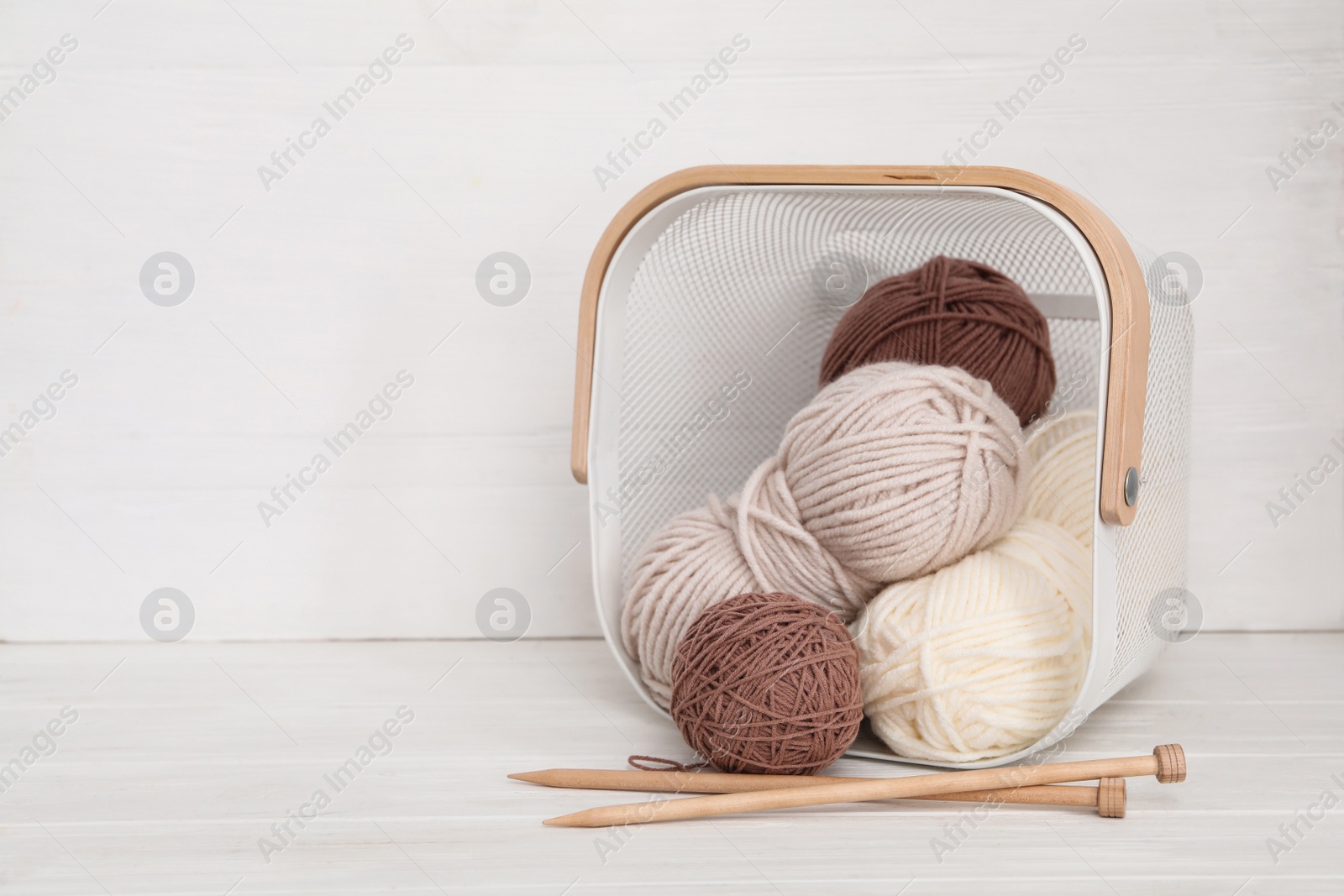 Photo of Woolen yarns in basket and knitting needles on white wooden table. Space for text