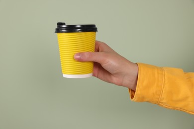 Photo of Woman holding takeaway cup with drink on pale green background, closeup. Coffee to go