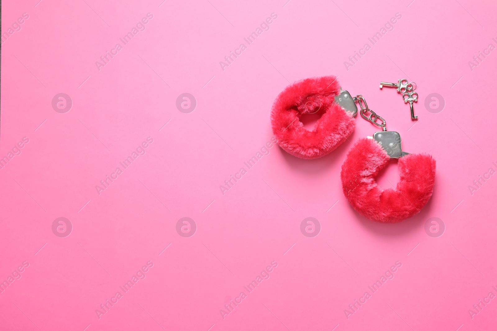 Photo of Red furry handcuffs and keys on pink background, flat lay with space for text. Sex toy