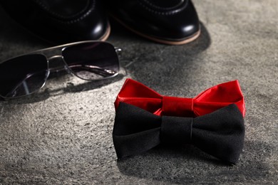 Photo of Stylish red bow tie and sunglasses on gray textured background