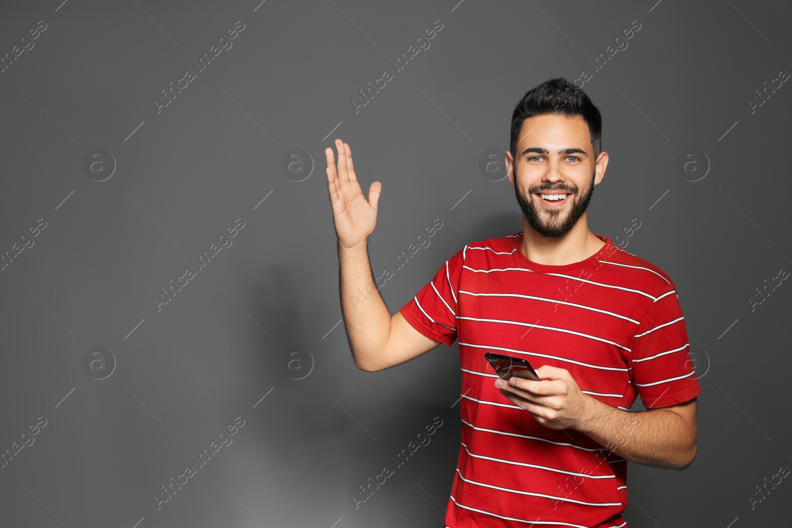 Photo of Portrait of handsome young man with mobile phone on gray background. Space for text