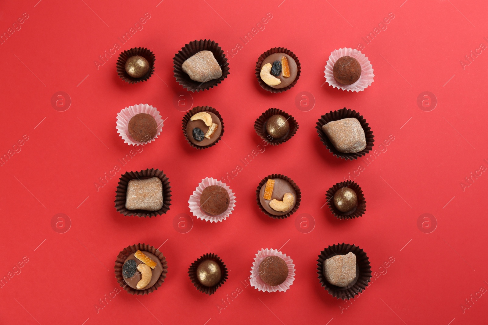 Photo of Different delicious chocolate candies on red background, flat lay