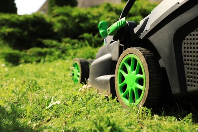 Photo of Lawn mower on green grass in garden, closeup. Space for text