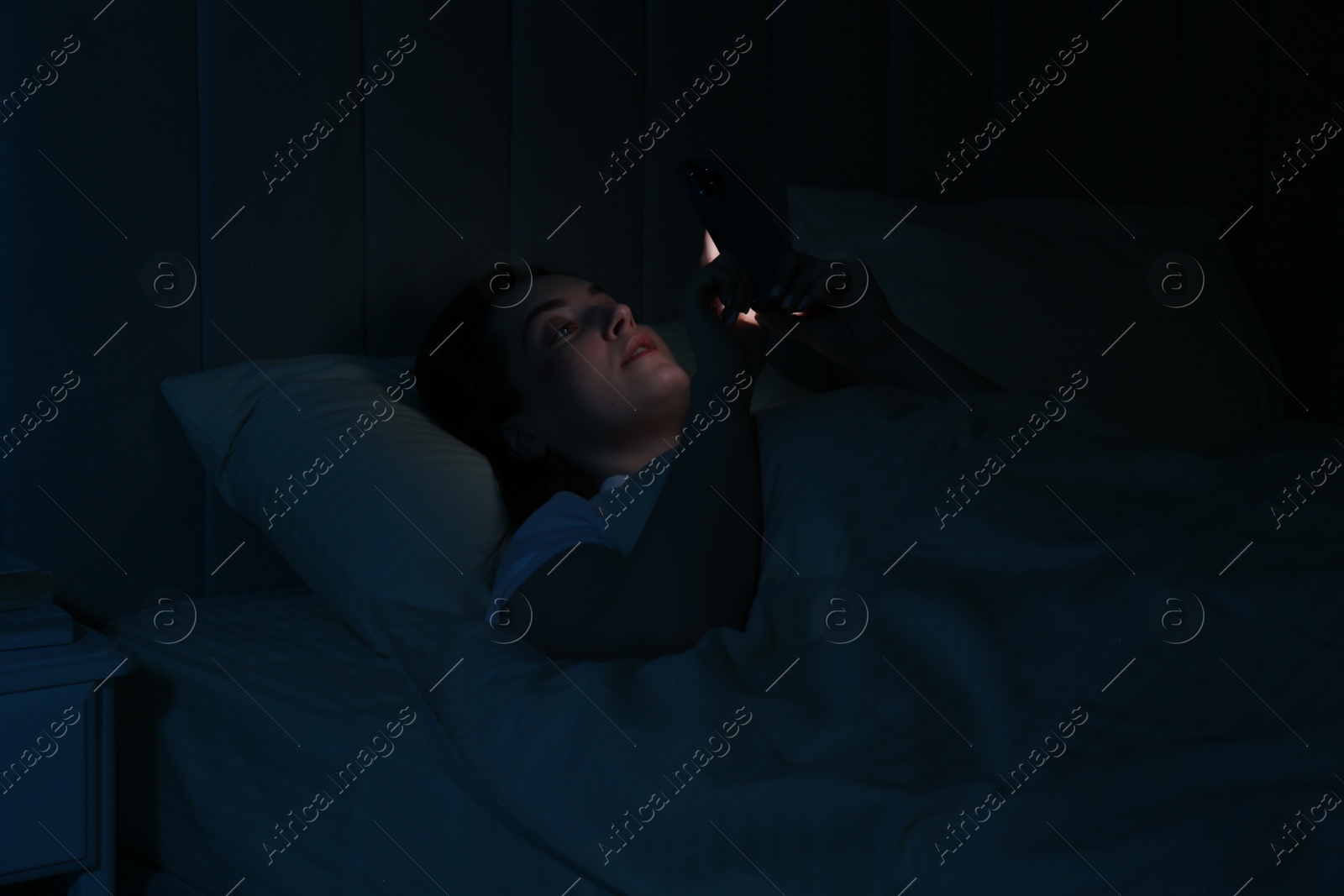 Photo of Woman using smartphone on bed at night. Internet addiction