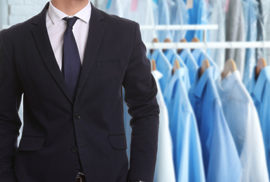 Businessman and rack with clean clothes at dry-cleaner's, closeup. Space for text 