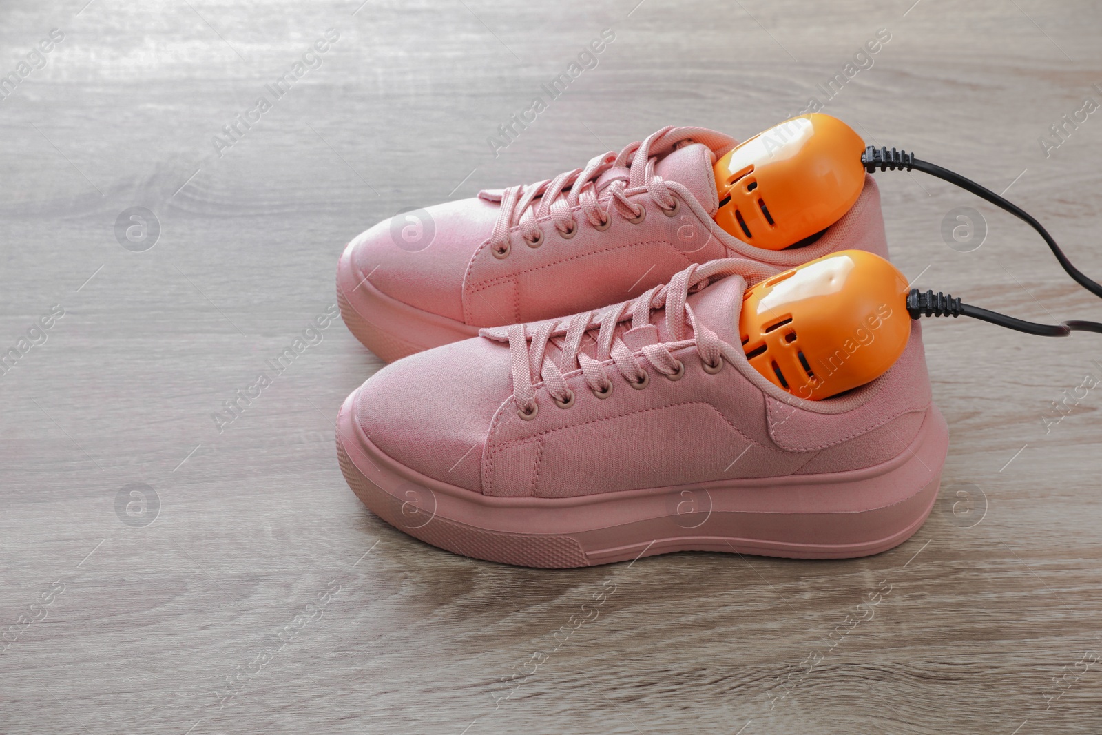 Photo of Pair of stylish sneakers with modern electric shoe dryer on wooden background