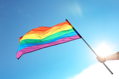 Gay man holding rainbow LGBT flag against blue sky