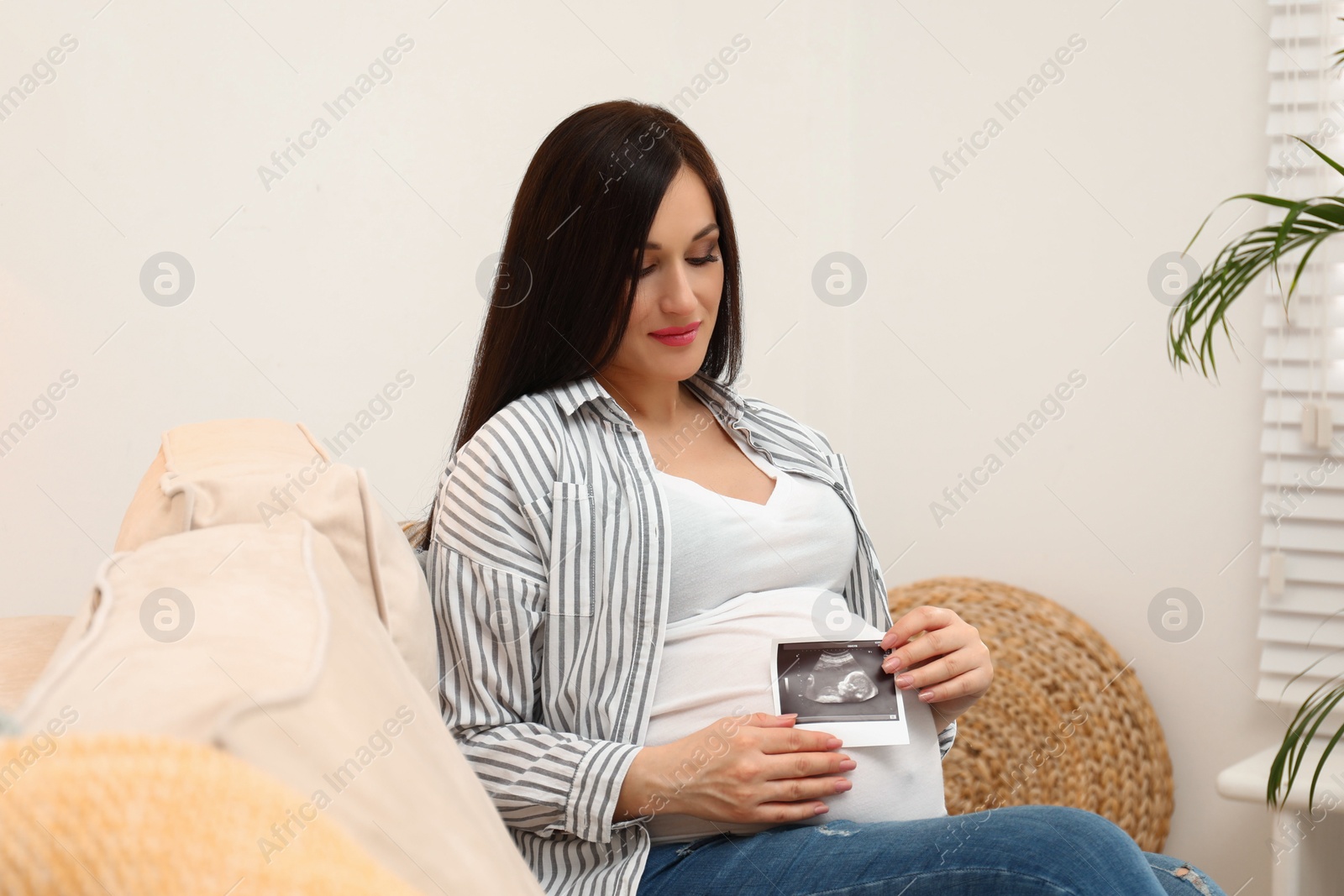 Photo of Beautiful pregnant woman with ultrasound photo of her baby at home