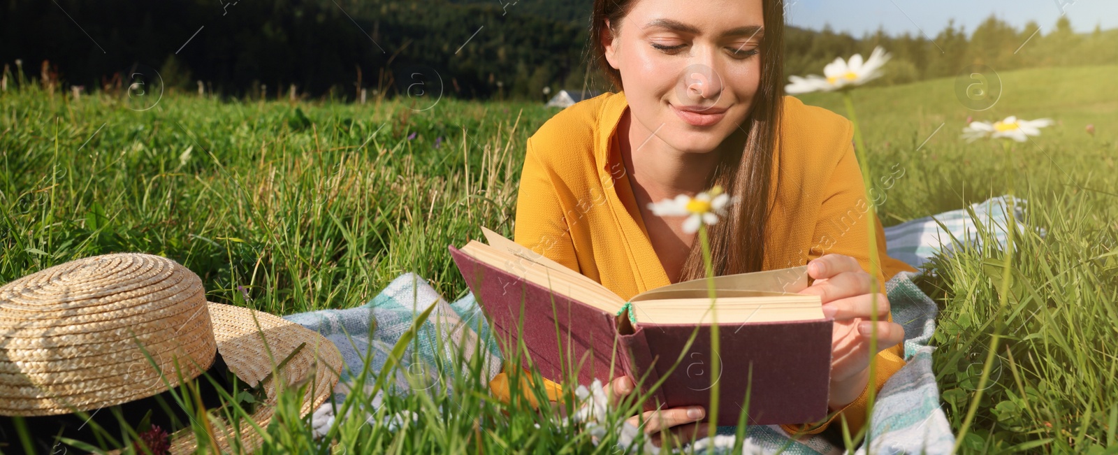 Image of Beautiful young woman reading book on green meadow in mountains. Banner design