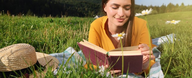 Image of Beautiful young woman reading book on green meadow in mountains. Banner design