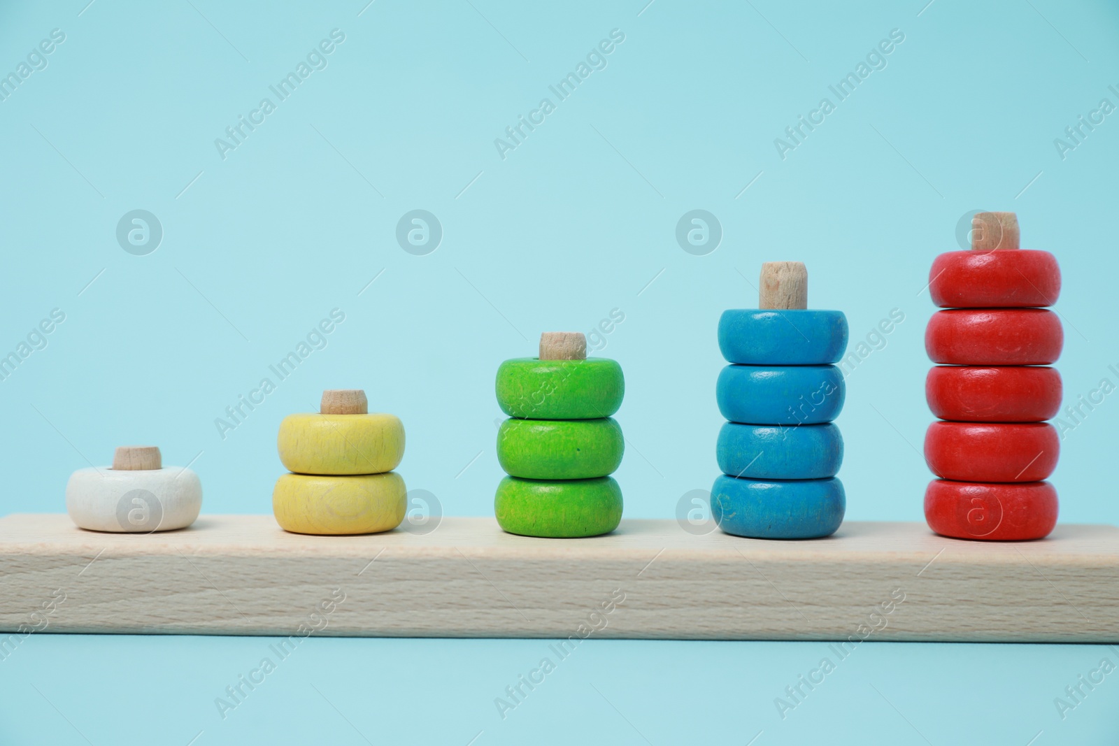 Photo of Stacking and counting game wooden pieces on light blue background. Educational toy for motor skills development