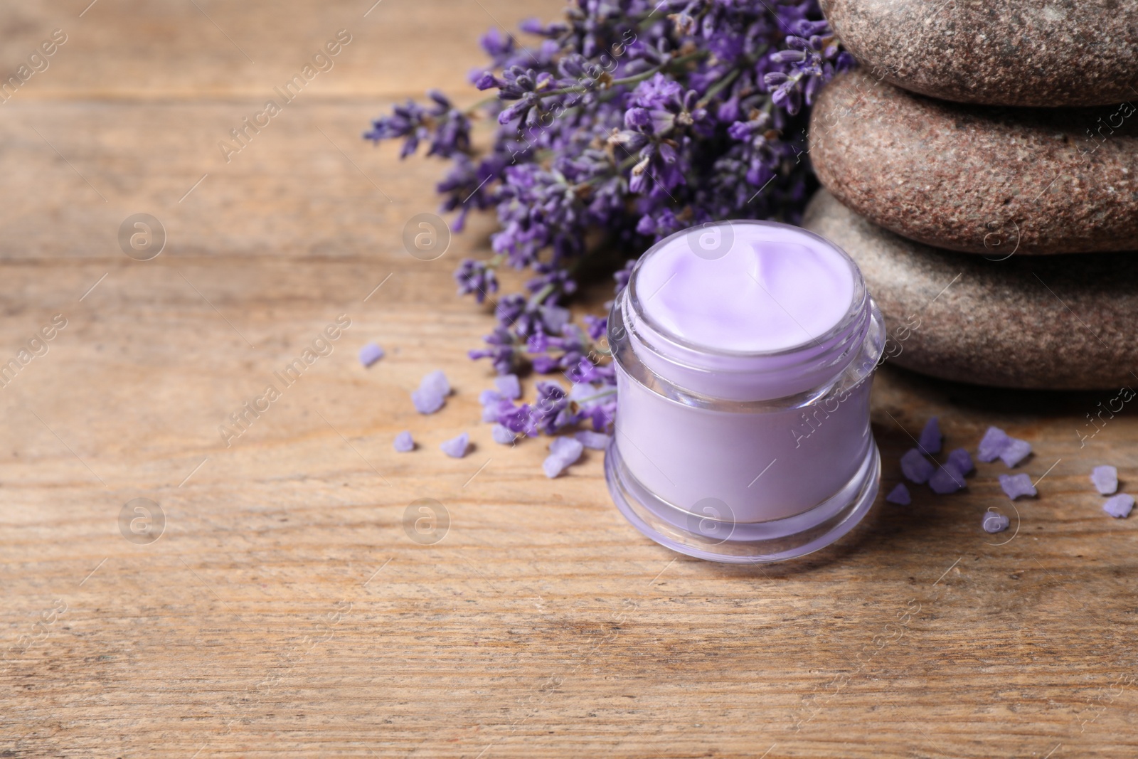 Photo of Stones, jar of cream and lavender flowers on wooden table. Space for text