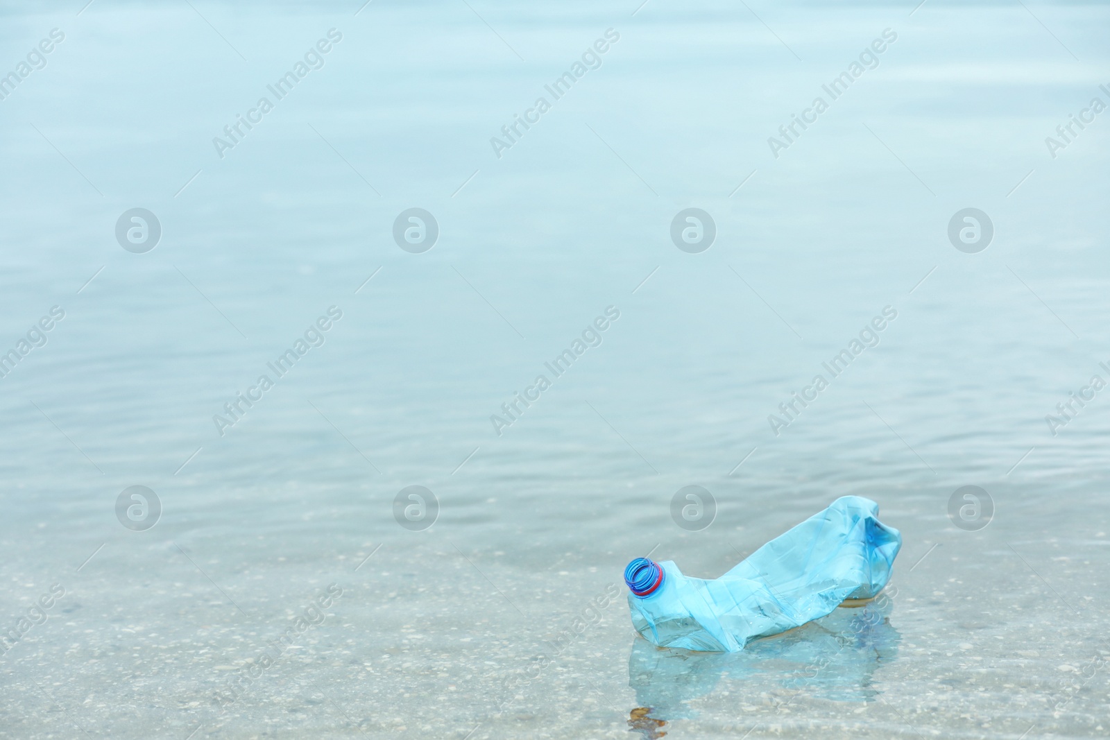 Photo of Used plastic bottle floating on water surface, space for text. Recycling problem