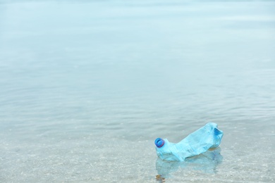 Photo of Used plastic bottle floating on water surface, space for text. Recycling problem