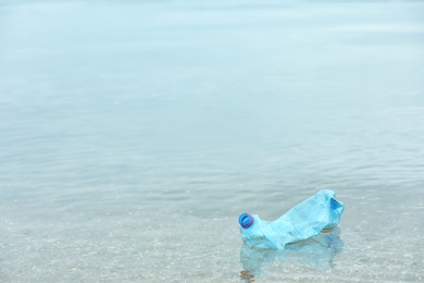 Used plastic bottle floating on water surface, space for text. Recycling problem