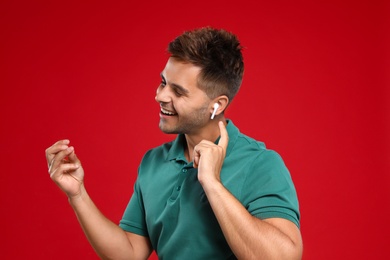 Happy young man listening to music through wireless earphones on red background