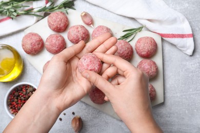 Woman making fresh raw meatballs at light grey table, top view