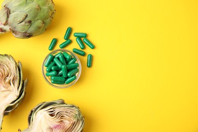 Photo of Bowl with pills and fresh artichokes on yellow background, flat lay. Space for text