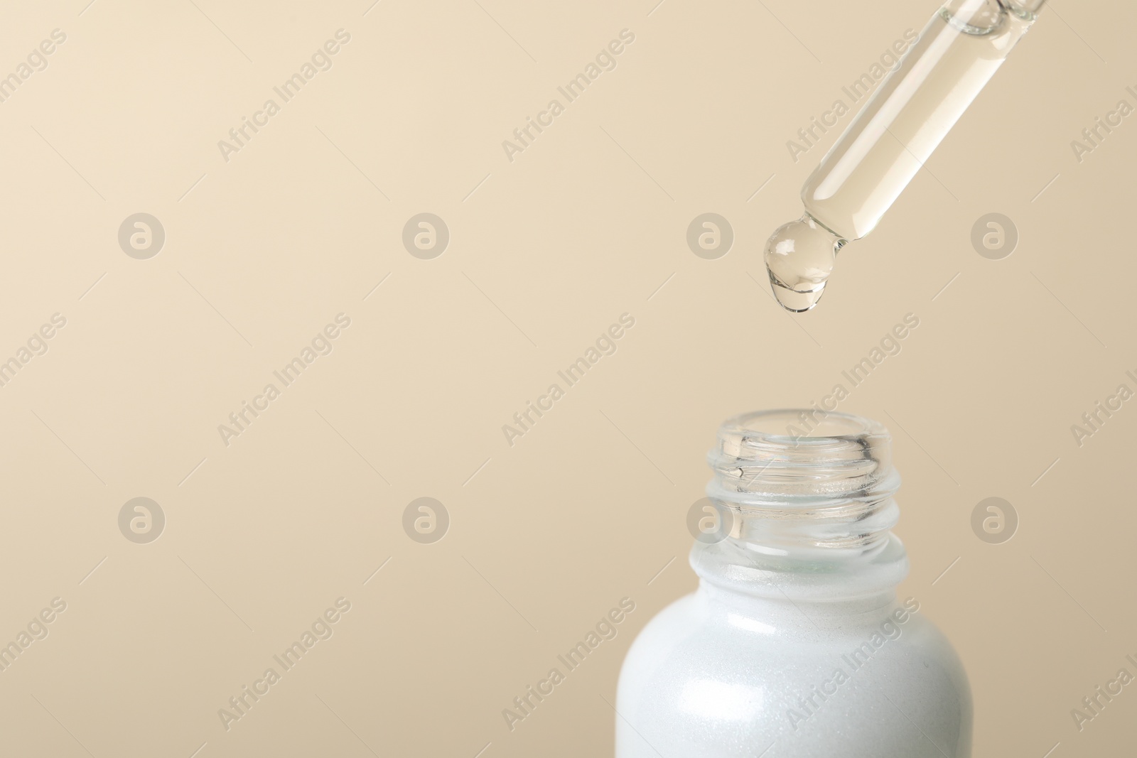 Photo of Dripping cosmetic serum from pipette into bottle on beige background, space for text