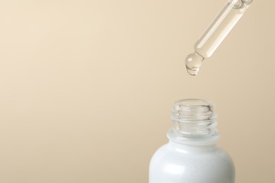 Photo of Dripping cosmetic serum from pipette into bottle on beige background, space for text